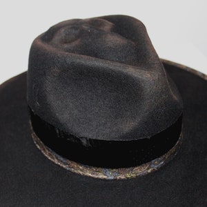 Puede incluir: Un sombrero fedora negro de ala ancha y una banda estampada alrededor de la corona.