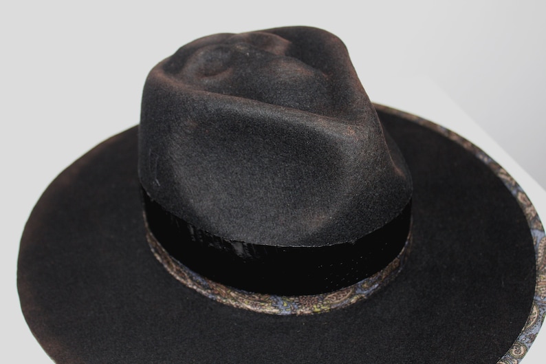 Puede incluir: Un sombrero fedora negro de ala ancha y una banda estampada alrededor de la corona.