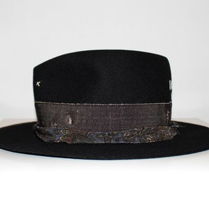 May include: A black felt fedora hat with a patterned band. The band is made of a dark blue fabric with a paisley design. The hat has a small white X stitched on the crown.