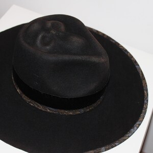 Puede incluir: Un sombrero fedora negro de ala ancha y una banda estampada alrededor de la corona.