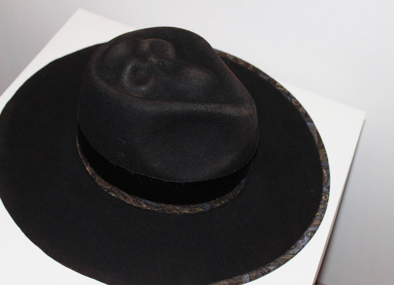 Puede incluir: Un sombrero fedora negro de ala ancha y una banda estampada alrededor de la corona.