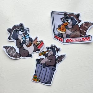 May include: Three stickers depicting cartoon raccoons. One is drinking from a cup, another eating pizza from a box, and the third is drinking from a bottle while sitting in a bin. The stickers have a white border.