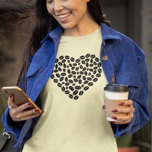 以下が含まれることがあります： コーヒー豆で作られたハートのデザインが特徴の、明るい黄色のTシャツ。青いジャケットを着て、コーヒーカップとスマートフォンを持っています。