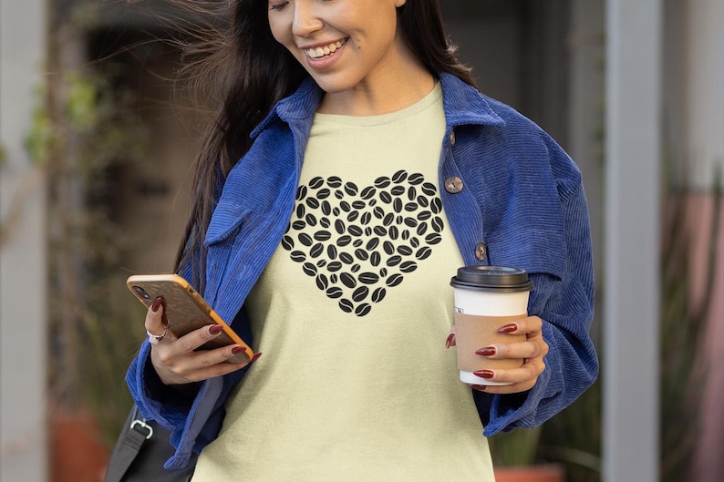 以下が含まれることがあります： コーヒー豆で作られたハートのデザインが特徴の、明るい黄色のTシャツ。青いジャケットを着て、コーヒーカップとスマートフォンを持っています。