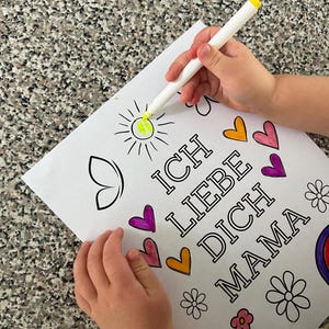 May include: A child's hand colors a sun with a yellow marker on a coloring page that says "Ich Liebe Dich Mama" with hearts and flowers.