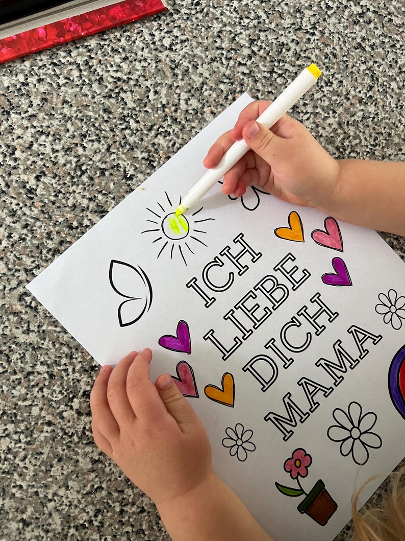 May include: A child's hand colors a sun with a yellow marker on a coloring page that says "Ich Liebe Dich Mama" with hearts and flowers.
