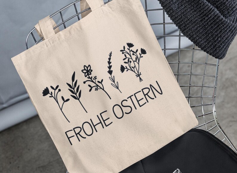 May include: A beige tote bag with black floral designs and the text "Frohe Ostern" printed on it.