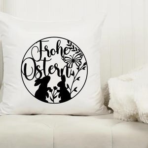 May include: White pillow with a black and white design of two bunnies, a butterfly, and the text "Frohe Ostern" in a circle.