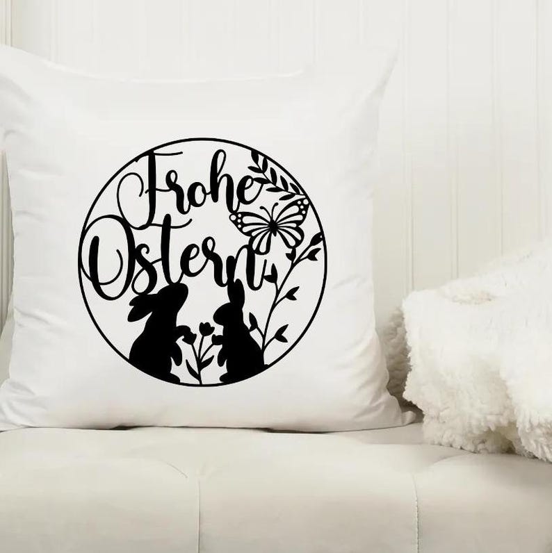 May include: White pillow with a black and white design of two bunnies, a butterfly, and the text "Frohe Ostern" in a circle.