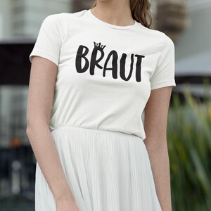 May include: White t-shirt with a black crown and the word "BRAUT" printed on the front.
