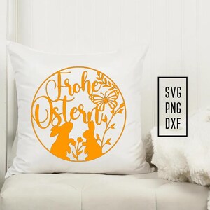 Puede incluir: Almohada blanca con un dise&ntilde;o redondo naranja con el texto "Frohe Ostern" con dos conejos y una mariposa. Se enumeran los formatos de archivo SVG, PNG y DXF.