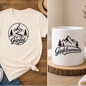 May include: A cream-colored t-shirt featuring a black circular graphic of a mountain, trees, and the text "Auf zum Gipfel" alongside a white ceramic mug displaying a black mountain graphic with the text "Gipfelmomente" in a script font.
