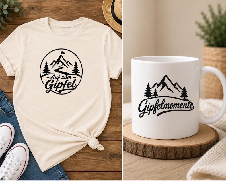 May include: A cream-colored t-shirt featuring a black circular graphic of a mountain, trees, and the text "Auf zum Gipfel" alongside a white ceramic mug displaying a black mountain graphic with the text "Gipfelmomente" in a script font.