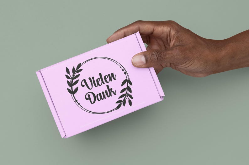 May include: A light pink rectangular cardboard shipping box featuring a black circular graphic design with two leafy branches on the sides and the German text "Vielen Dank" printed in a stylised script font in the centre of the circle.