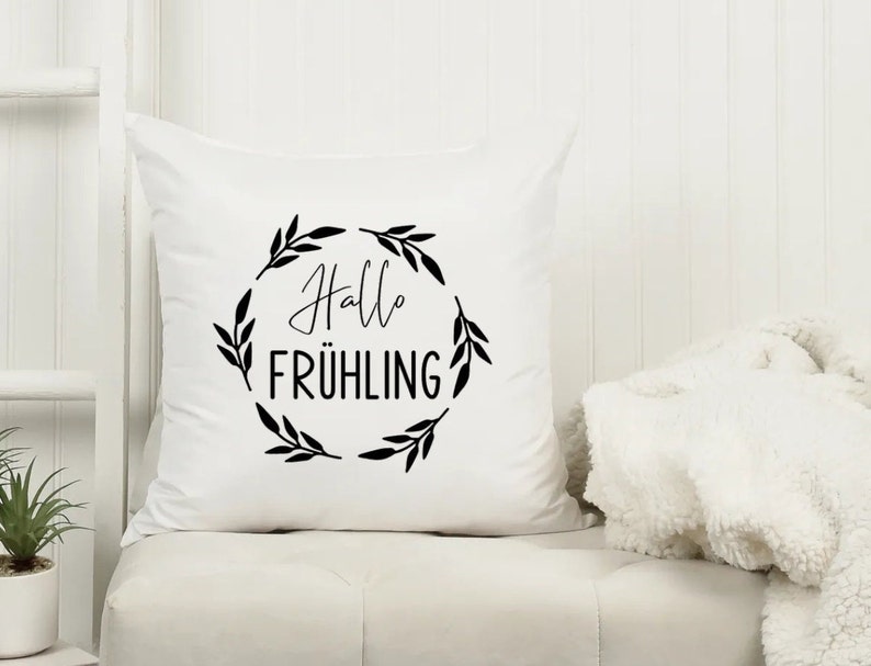 May include: White throw pillow with black text and a wreath of leaves that says "Hallo Fr&uuml;hling".