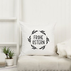 Peut inclure: Oreiller blanc avec du texte noir et un motif de couronne qui dit "Frohe Ostern" qui signifie "Joyeuses P&acirc;ques" en allemand.