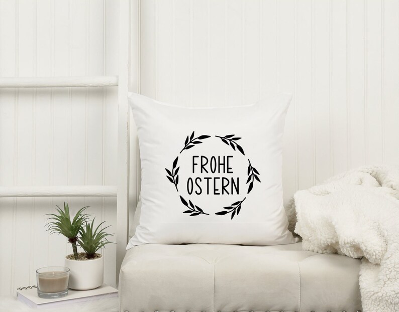 Peut inclure: Oreiller blanc avec du texte noir et un motif de couronne qui dit "Frohe Ostern" qui signifie "Joyeuses P&acirc;ques" en allemand.