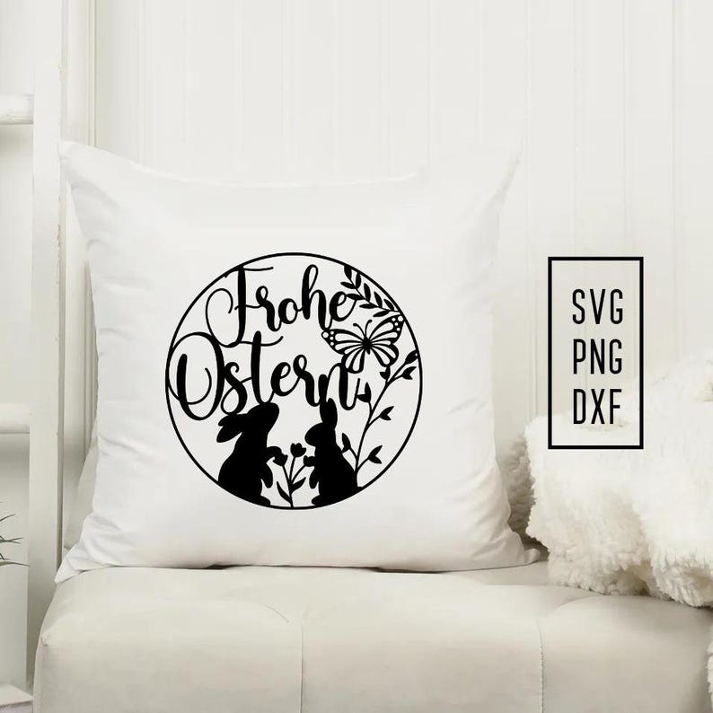 Puede incluir: Almohada blanca con texto negro que dice "Frohe Ostern" en un c&iacute;rculo con dos conejos y una mariposa.