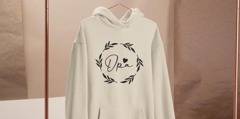 May include: A white hoodie with a black design of a wreath with the word "Opa" and a small heart in the centre.