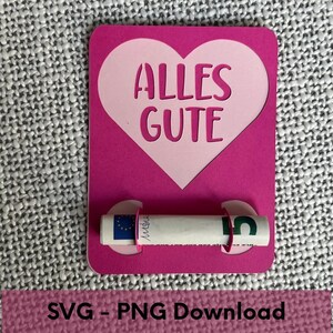 K&ouml;nnte beinhalten: Rosa Karte mit einem gro&szlig;en rosa Herz, das in der Mitte ausgeschnitten ist. Das Herz tr&auml;gt den Text "ALLES GUTE" in Wei&szlig;. Ein zusammengerollter Geldschein wird von zwei rosa Kreisen auf der Karte gehalten.