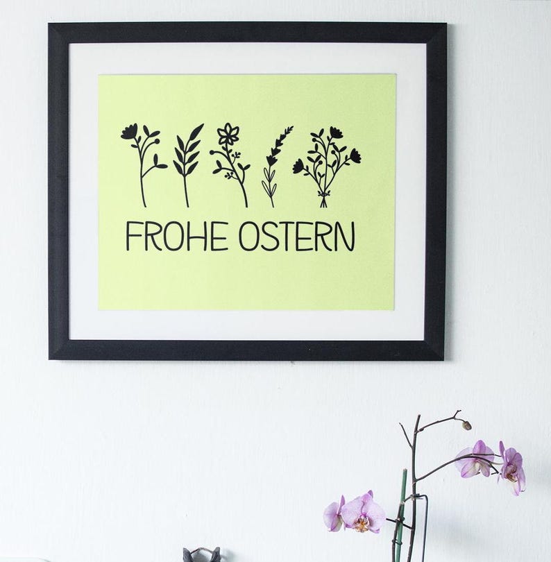 May include: A framed print with a light green background and black silhouettes of flowers. The text "FROHE OSTERN" is printed in black below the flowers.
