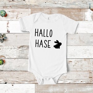 Peut inclure: Combinaison blanche pour b&eacute;b&eacute; avec le texte noir "Hallo Hase" et une silhouette noire de lapin.