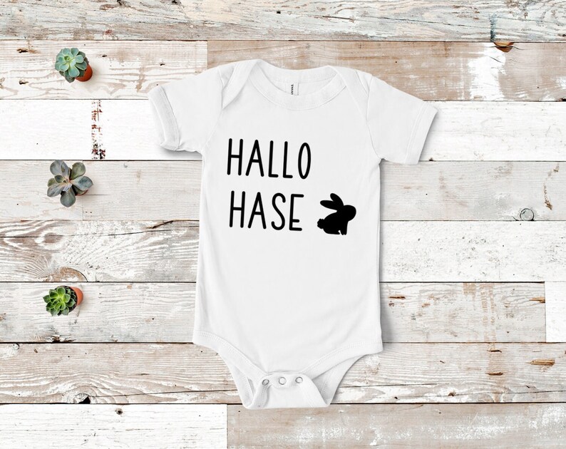 Peut inclure: Combinaison blanche pour b&eacute;b&eacute; avec le texte noir "Hallo Hase" et une silhouette noire de lapin.