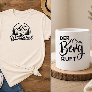 May include: A cream-colored t-shirt featuring a black graphic of mountains, pine trees, and the sun with the text "Wanderlust" and a white ceramic mug featuring a black graphic of mountains and the text "DER BERG RUFT" in a bold font.