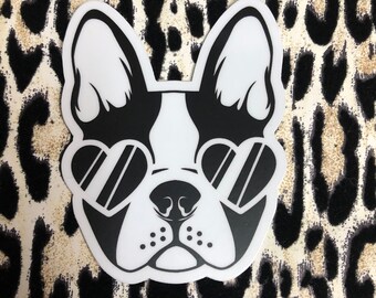 May include: A black and white sticker featuring a French bulldog with heart-shaped sunglasses. The sticker has a white background and is set against a leopard print background.