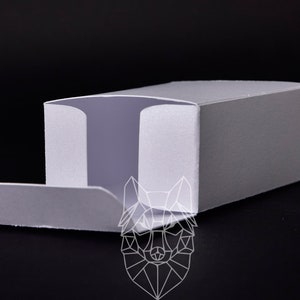 Könnte beinhalten: Eine rechteckige, offene, graue Box mit strukturierter Oberfläche. Die Box hat einen teilweise geöffneten Deckel, der einen hellvioletten Innenraum freilegt. Ein geometrisches Wolfskopf-Logo ist sichtbar.
