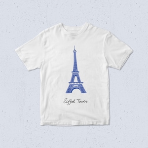 May include: White t-shirt with a blue illustration of the Eiffel Tower. The words "Eiffel Tower" are written in a script font beneath the image. The shirt has short sleeves and a round neck.