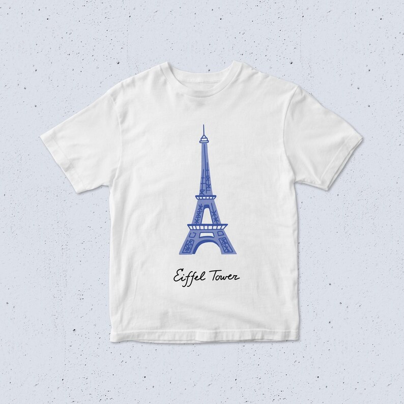 May include: White t-shirt with a blue illustration of the Eiffel Tower. The words "Eiffel Tower" are written in a script font beneath the image. The shirt has short sleeves and a round neck.