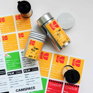 Puede incluir: Un conjunto de botes de película Kodak, rollos de película y etiquetas. Los botes son plateados con etiquetas Kodak amarillas y rojas. Las etiquetas son naranjas, verdes y rojas, con espacios para información. El texto "Ocean ISO 400" está escrito a mano.