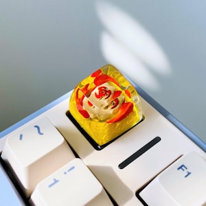 May include: A custom keyboard keycap featuring a koi fish design. The keycap has a yellow base with a clear resin top, showcasing a detailed koi fish in red and white. The keycap is installed on a white keyboard.