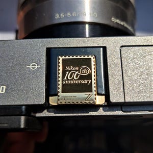 Puede incluir: Una cámara negra con una inscripción dorada que dice "Nikon 100 aniversario".