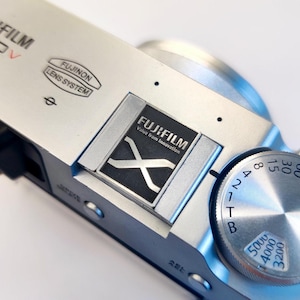 May include: A silver camera with a black Fujifilm logo and the text "Value from Innovation". The camera has a silver dial with numbers and letters.