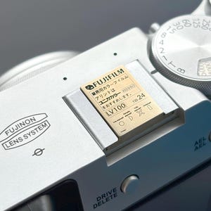 May include: A silver camera with a gold film cartridge that reads "FUJIFILM 業務用カラーフィルム アリントは ユニカカラー 2023/6/2 をおすすめします。 LV100 135-24".