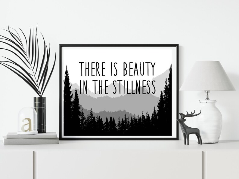 May include: Black and white print with a mountain range silhouette and the text "THERE IS BEAUTY IN THE STILLNESS".
