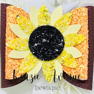 May include: A brown, orange, and yellow glitter sunflower hair bow with the text "Kenzie Avenue boutique" on the bottom.