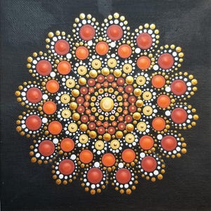 May include: A square canvas painting featuring a central mandala design created with raised dot art. The pattern consists of concentric circles of dots in shades of orange, metallic gold, cream, and white, all set against a solid black background.