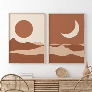 May include: Two framed abstract art prints. One features a sun over layered brown and beige shapes. The other depicts a crescent moon over similar shapes. The prints are displayed above a wooden cabinet with woven chairs and a rug.