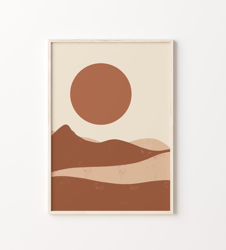 May include: Abstract art print featuring a minimalist landscape with a large, rust-colored sun and layered, earthy-toned hills. The artwork is framed in a light wood frame, creating a warm and inviting aesthetic. The color palette includes shades of beige, brown, and rust.