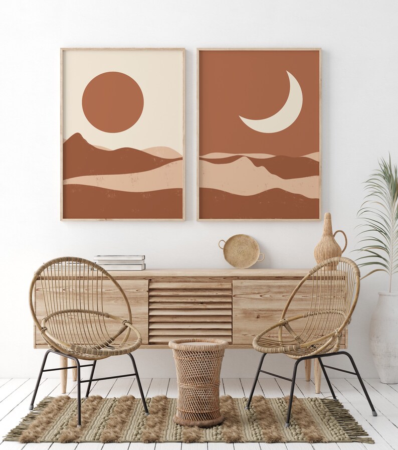 May include: Two framed abstract art prints. One features a sun over layered brown and beige shapes. The other depicts a crescent moon over similar shapes. The prints are displayed above a wooden cabinet with woven chairs and a rug.