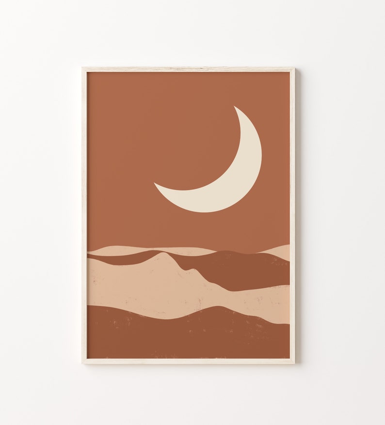 May include: Abstract art print featuring a crescent moon and desert landscape in shades of brown and beige. The artwork is framed in a light wood frame, suitable for home decor.
