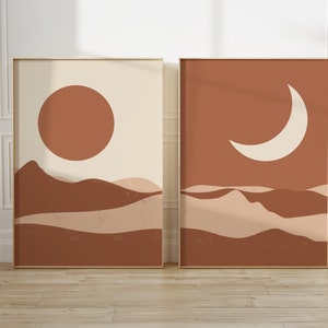 May include: Two framed art prints with a minimalist desert landscape design. One features a large orange sun over brown hills against a cream background. The other shows a white crescent moon over similar hills.