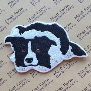 May include: An embroidered patch of a border collie dog, black and white with brown eyes. The dog is lying down with its head turned to the side and its paws are visible.