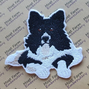 May include: Black and white embroidered patch of a border collie dog with its head tilted and tongue sticking out.