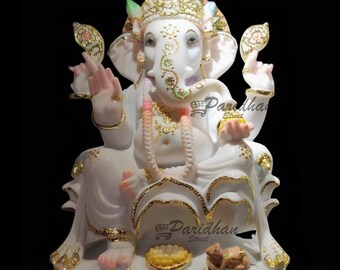 May include: A white and gold statue of the Hindu deity Ganesha, seated in a lotus position. The statue features intricate gold detailing on the crown, jewelry, and clothing. The elephant-headed figure has multiple arms and is holding various objects. A small mouse is at the base.