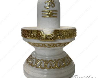 May include: White marble Shiva Lingam statue with gold accents. The statue is on a white marble base with gold accents. The statue is a traditional Hindu religious symbol.