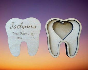May include: A wooden tooth-shaped box with the inscription "Jaelynn's Tooth Fairy Box" and a small star with a wand. The box has a heart-shaped opening on the other side.